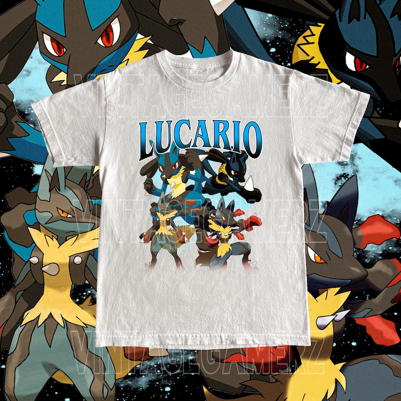 May include: A light gray t-shirt featuring the word "LUCARIO" in blue, with a graphic of multiple Lucario characters in various poses. The design includes blue, black, yellow, and red accents. The shirt has a crew neck and short sleeves.