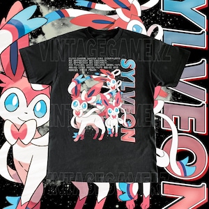 May include: Black t-shirt featuring a Sylveon graphic with pink, white, and blue accents. The design includes the word "SYLVEON" in a vertical font and Japanese text. The shirt has a vintage gamer aesthetic.