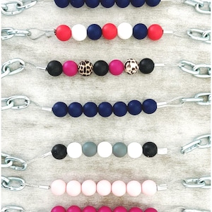 May include: Rows of colorful beads in various color combinations, strung on silver wire and attached to a silver chain. Bead colors include navy, red, white, pink, black, gray, and leopard print.
