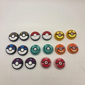 May include: A collection of sixteen colorful, circular game console accessories. The accessories feature various designs, including red and white, yellow and black, blue and white, teal and white, orange and white, purple and white, and pink and red.