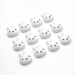 May include: A collection of white bunny-shaped objects with black dot eyes and cross-shaped mouths. The objects are arranged on a white background. The bunnies have rounded bodies and upright ears.