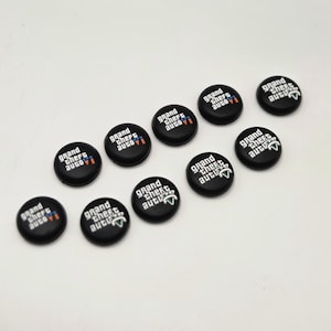 May include: A set of ten circular black thumbstick covers for a game controller. Each cover features the white text Grand Theft Auto VI with a small orange Roman numeral VI. The covers are arranged in two rows of five on a plain white surface.