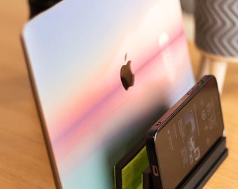 Könnte beinhalten: Ein schwarzer Telefonständer mit grünem Filzeinsatz hält ein schwarzes Smartphone, dessen Bildschirm eine Wetter-App anzeigt. Ein Laptop mit einem farbenfrohen Sonnenuntergangsdesign ist gegen den Ständer gelehnt.