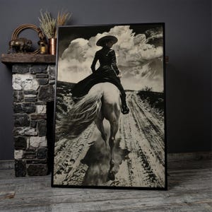 May include: Black and white framed print of a person riding a white horse on a dirt road. The person is wearing a hat and long coat. The sky is filled with dramatic clouds. The print is displayed on a wooden floor.