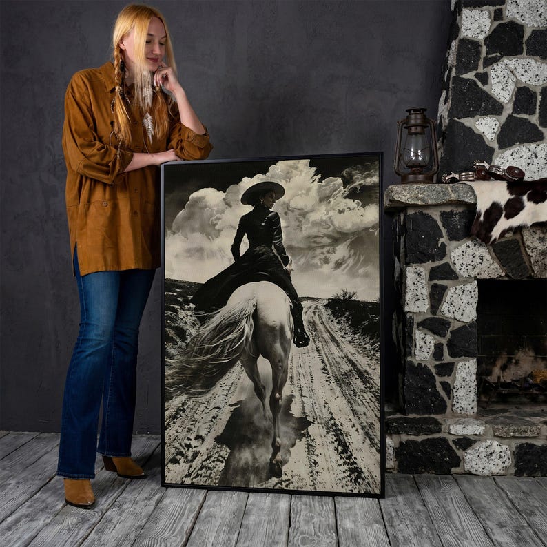 May include: Black and white framed art print depicting a person on horseback riding down a dirt road. The rider is wearing a hat and long coat. The background features a cloudy sky. The art is displayed next to a person wearing a brown shirt and blue jeans.