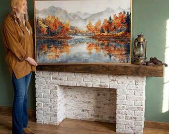 Könnte beinhalten: Ein gerahmtes Landschaftsgemälde zeigt eine ruhige Seeszene mit Herbstlaub. Das Kunstwerk hat einen goldenen Rahmen und zeigt leuchtend orange, rote und gelbe Bäume, die sich im Wasser spiegeln. Berge sind im Hintergrund zu sehen und schaffen eine friedliche Atmosphäre.