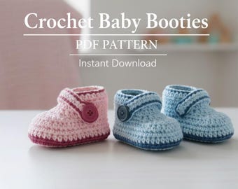 Op de afbeelding: Haakpatroon voor babyslofjes. De afbeelding toont twee babyslofjes, één roze en één blauw, met knoopsluitingen. De slofjes zijn handgemaakt en liggen op een wit oppervlak. De tekst "Crochet Baby Booties PDF Pattern Instant Download" staat bovenaan.