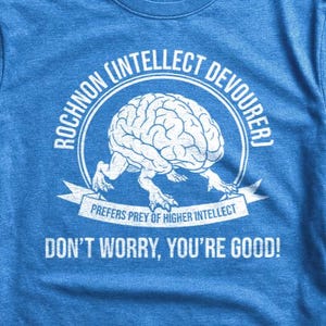 May include: A blue t-shirt with a white graphic of a brain with legs, encircled by the words "ROCHNON INTELLECT DEVOURER". Below the brain is the text "PREFERS PREY OF HIGHER INTELLECT" and "DON'T WORRY, YOU'RE GOOD!"