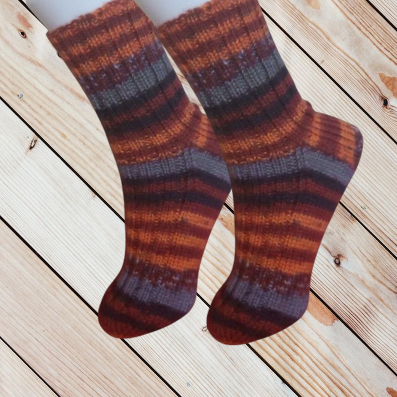 May include: A pair of hand-knitted socks with a striped pattern in shades of orange, burgundy, and gray. The socks are displayed against a wooden background. The socks appear to be made of a soft, warm yarn.