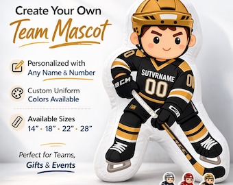 Könnte beinhalten: Ein Hockey-Teammaskottchen-Kissen in schwarz-goldener Uniform, das einen Hockeyschläger hält. Das Kissen ist mit jedem Namen und jeder Nummer anpassbar. Verfügbare Größen: 35,5 cm, 45,7 cm, 55,8 cm und 71,1 cm. Das Bild zeigt auch drei kleinere Hockey-Spieler-Anstecknadeln.