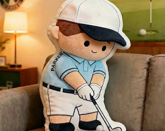 Könnte beinhalten: Ein Golf-Kissen in Form eines Cartoon-Golfers. Der Golfer trägt eine weiße Kappe mit marineblauem Schirm, ein hellblaues Poloshirt und eine weiße Hose. Der Name "PARKER" steht auf dem Ärmel. Der Golfer hält einen Golfschläger und ist bereit, einen Ball zu schlagen.
