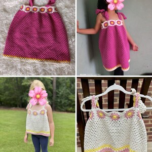 May include: Handmade crochet top and dress in pink, white, and yellow. The top and dress feature a floral design along the neckline and straps. The dress has tie straps and a scalloped hem. The top is shown on a hanger and worn by a child.