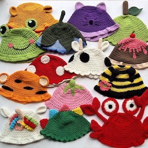 Puede incluir: Una colección de coloridos sombreros de ganchillo hechos a mano con varios diseños de animales y alimentos. Los sombreros incluyen una rana, un oso, una seta, una abeja, un cangrejo y más. Cada sombrero presenta detalles únicos y colores vibrantes.