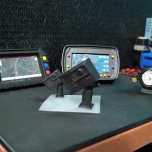 May include: Four black dashboard gauges with various displays, including a map, speedometer, and other readings. The gauges are mounted on a black surface.