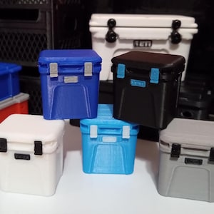 May include: A collection of six miniature coolers in various colors, including blue, black, white, and gray. The coolers are all the same size and shape, and they are arranged in a row on a table.