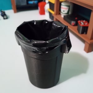 May include: A black plastic trash can with a black plastic trash bag inside. The trash can is empty.