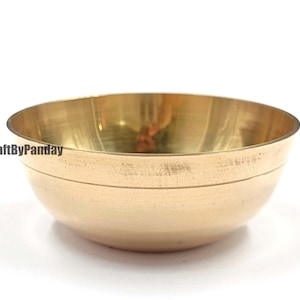 May include: A golden brass bowl with a rounded shape. The bowl has a smooth, polished surface and a subtle band detail near the top. The CraftByPanday logo is visible on the side of the bowl. The bowl is set against a white background.