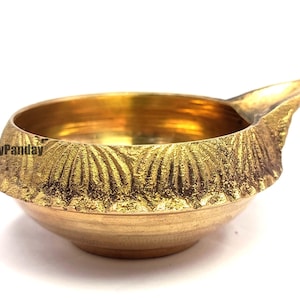 May include: A gold-coloured brass bowl with a textured rim and a small spout. The bowl has a smooth interior and a decorative, textured exterior. The bowl is likely used for religious or decorative purposes.