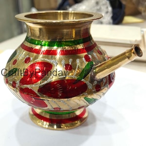 May include: A gold-colored metal water pot with a spout, decorated with red and green painted floral designs. The pot has a wide rim and a round base. The text "CraftByPanday" is visible on the side.