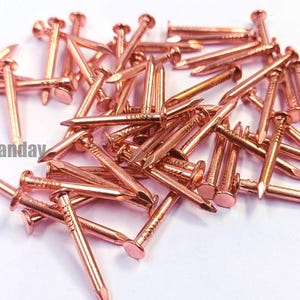 May include: A pile of copper-colored nails with flat heads and pointed tips. The nails are scattered across a white surface. The text "CraftByPanday" is visible in the lower left corner.