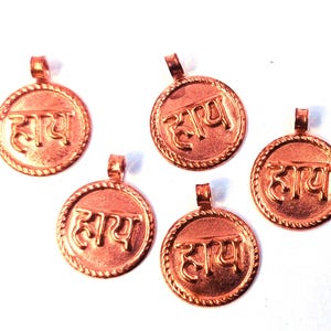 May include: Five copper-colored round pendants. Each pendant has a raised border and a loop at the top. The word "हाय" is embossed in the center of each pendant.