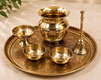 May include: A polished brass set consisting of a large circular tray with an embossed floral pattern, a central pot, a tall hand bell, a small oil lamp, and two small bowls. All items feature a reflective metallic gold finish and smooth surfaces.