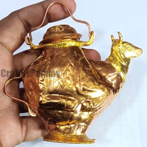 May include: A handcrafted, gold-coloured metal decorative teapot with a cow-shaped spout. The teapot features intricate embossed patterns and a copper handle. The design includes a small lid and a base, showcasing a unique blend of artistry and functionality.