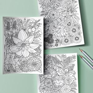 May include: Three black and white floral coloring pages with intricate designs of various flowers and foliage. Two gray pencils are placed on a light green surface, suggesting a creative activity. The pages are ready for coloring.