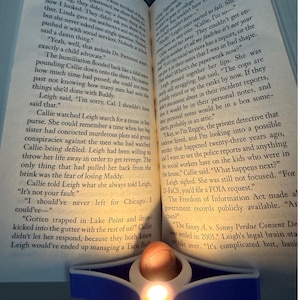 May include: An open book with text, illuminated by a small candle. The pages display printed text, with the numbers 190 and 191 visible. The candle's warm glow highlights the book's pages, creating a cozy atmosphere.