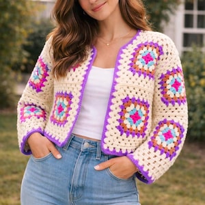 May include: Cream-colored crochet jacket with square, colorful patterns in pink, blue, orange, and purple. The jacket has a purple trim and is worn with a white top and blue jeans. The jacket is a cropped style.