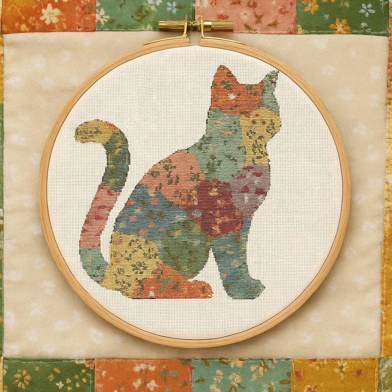 Pu&ograve; includere: Un disegno di gatto a punto croce in un telaio da ricamo in legno. Il gatto &egrave; composto da toppe di tessuto colorate nei toni dell'arancione, verde, blu e giallo. Il telaio &egrave; posto su uno sfondo patchwork con motivi floreali.