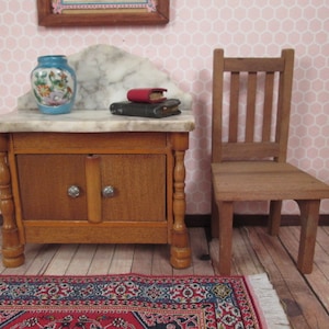 May include: Miniature wooden furniture set featuring a small cabinet with a marble top, a blue vase with floral designs, and a wooden chair. The cabinet has two doors with silver knobs. A small rug is in the foreground.