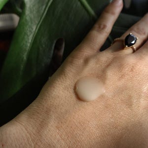 May include: A close-up of a hand with a clear, viscous liquid on the palm. The liquid is slightly pearlescent and has a smooth, even texture. The hand is wearing a gold ring with a black gemstone.