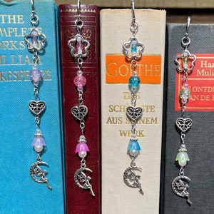 May include: Three silver bookmark chains with different coloured beads and charms. Each chain features a flower charm, a heart charm, a bell charm, and a crescent moon charm with a fairy. The beads are pink, blue, and green.