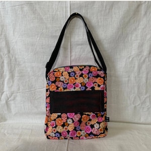 May include: A black shoulder bag with a floral print featuring pink, orange, and yellow flowers. The bag has a black mesh pocket on the front.