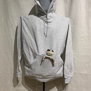 Op de afbeelding: Een grijs hoodie met een klein knuffeldier in de zak.