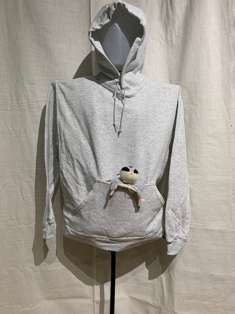 Op de afbeelding: Een grijs hoodie met een klein knuffeldier in de zak.