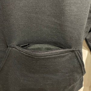 Op de afbeelding: Zwarte hoodie met een ritszak op de voorkant.