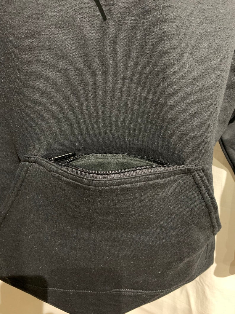Op de afbeelding: Zwarte hoodie met een ritszak op de voorkant.