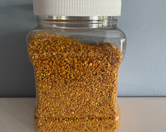 May include: A clear plastic jar filled with yellow bee pollen granules. The jar has a white lid.