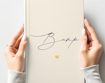 May include: A cream-colored journal with the word "Bump" in elegant script and a small gold heart. The journal is held by two hands with manicured nails, suggesting a pregnancy or baby-related theme.