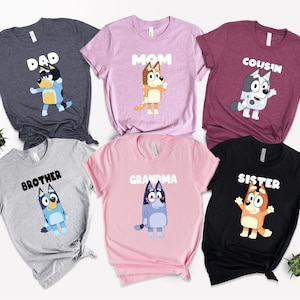May include: Assorted-color graphic t-shirts featuring cartoon characters and family-related text. The shirts are in various colors, including gray, pink, and black. Text includes "Dad," "Mom," "Cousin," "Brother," "Grandma," and "Sister."