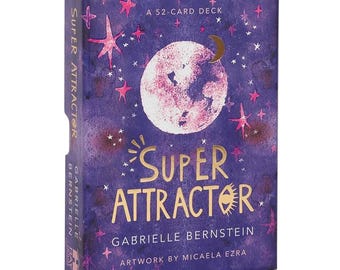 May include: A purple card deck box with gold lettering and a celestial design. The box reads "SUPER ATTRACTOR" and "GABRIELLE BERNSTEIN". The artwork features a pink and white moon, stars, and a crescent moon. The text "A 52-CARD DECK" is also visible.