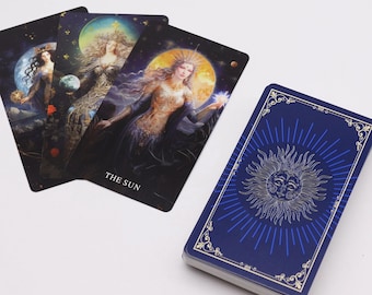 May include: A deck of tarot cards with a navy blue back featuring a sun design and a gold border. Three cards are fanned out, displaying illustrations of women with celestial backgrounds. One card reads "THE SUN."