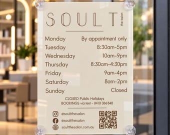 May include: A rectangular cream-colored sign attached to a glass door with four suction cups. It displays the text SOULT the salon, weekly operating hours, a notice for public holidays, a booking phone number, social media handles, and a QR code.