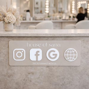 Op de afbeelding: Een rechthoekig beige bord met de tekst house of sana en de zin TAP TO CONNECT WITH US. Het bevat witte iconen voor Instagram, Facebook, Google en een wereldbol, ontworpen voor digitale interactie op een gestructureerd oppervlak.