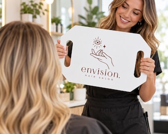 May include: A white rectangular hair coloring board with two side handles, featuring a dark brown graphic of an open hand holding an eye with rays and the text envision. HAIR SALON printed in a clean, sans-serif font on the front surface.