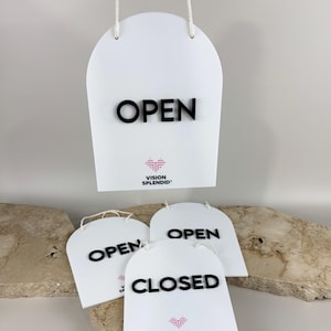 May include: A white arched sign with the black text OPEN, featuring a pink heart logo and the text VISION SPLENDID. Below are two additional white arched signs, one with the black text OPEN and one with the black text CLOSED.