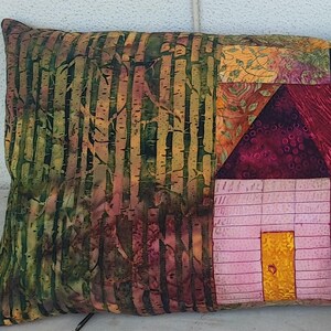 Puede incluir: Una almohada decorativa con un diseño de patchwork que presenta una casa con un exterior rosa y blanco y una puerta amarilla. El fondo de la almohada es una tela verde y marrón con un patrón de abedul.