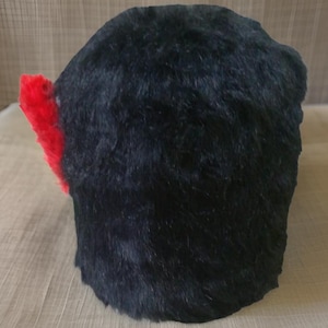Może przedstawiać: Czarny, puszysty kapelusz z czerwonym pomponem na górze.